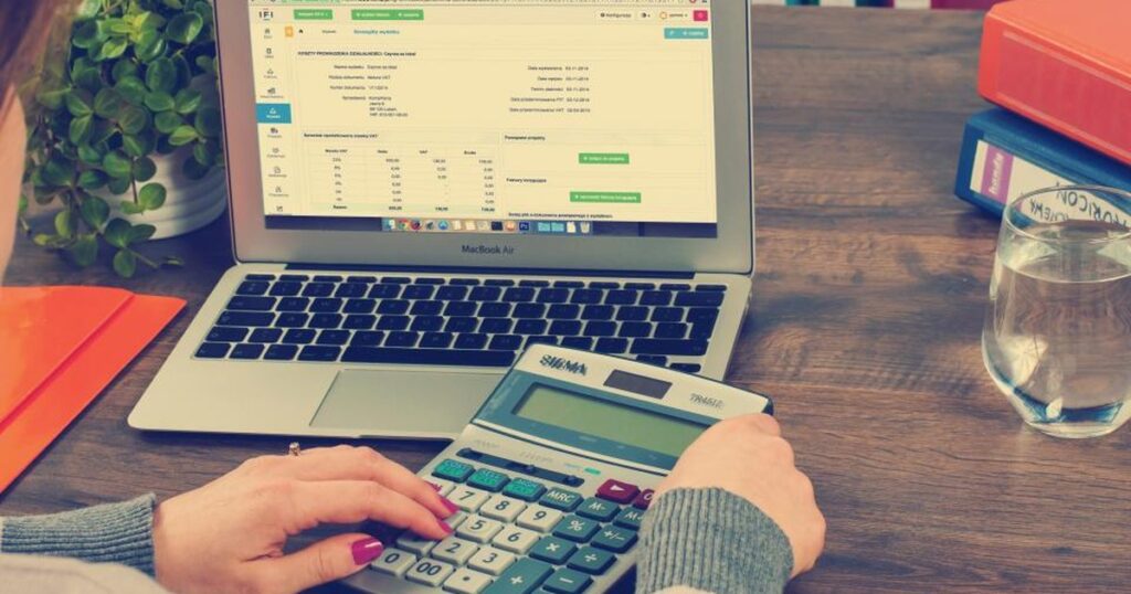 Accountant checking VAT input tax figures on a calculator and laptop