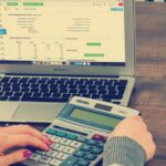 Accountant checking VAT input tax figures on a calculator and laptop